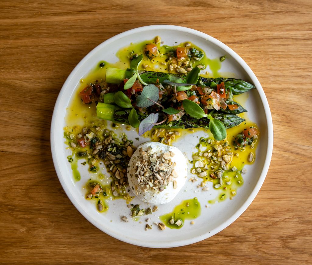 New Season asparagus dish with creamy goats curd, sauce vierge, toasted seeds, wild garlic on the plate on a table