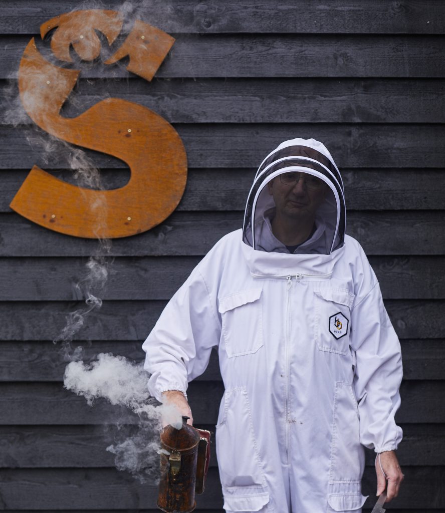 David the beekeeper in his protective beekeeping suit holding a bee smoker